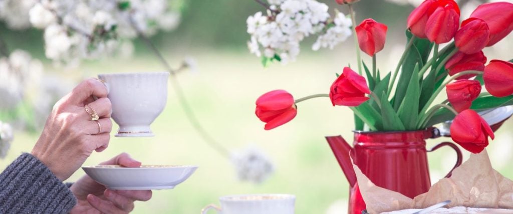 A picture of someone holding a tea cup next to a pot of flowers: how to prepare for spring 