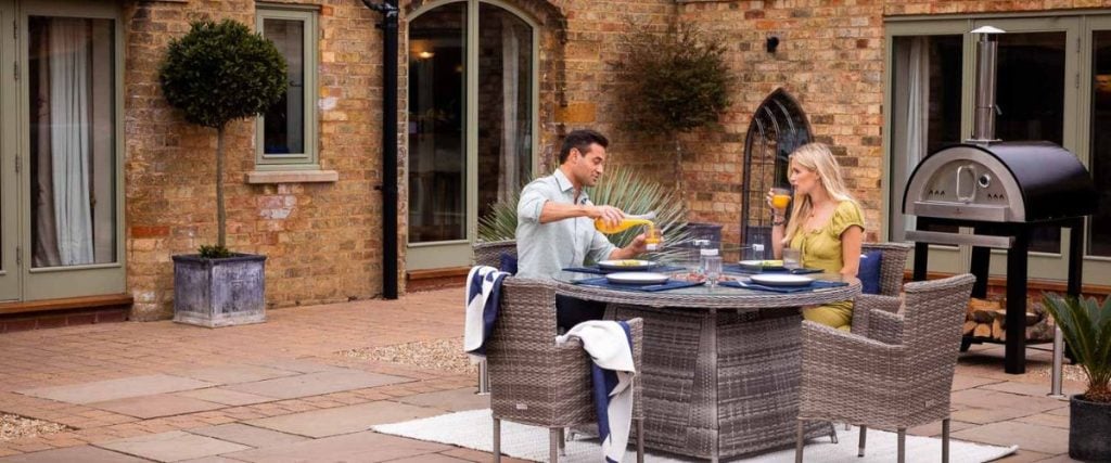 A picture of a couple enjoying a meal in the garden on their garden furniture: round dining tables
