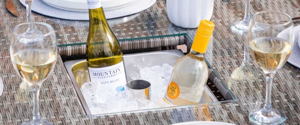 A picture of wine glasses and some wine in ice in a rattan dining table's drinks cooler: outdoor furniture features